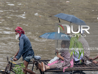 Passengers are riding on a rickshaw to go through a waterlogged street after heavy rain in Dhaka, Bangladesh, on July 12, 2024. (