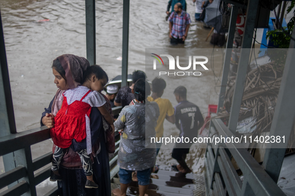 People are getting stuck on a footbridge after heavy rain is causing a waterlogged street in Dhaka, Bangladesh, on July 12, 2024. 