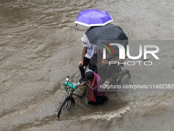 Passengers are riding on a rickshaw to go through a waterlogged street after heavy rain in Dhaka, Bangladesh, on July 12, 2024. (