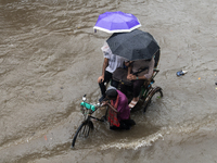 Passengers are riding on a rickshaw to go through a waterlogged street after heavy rain in Dhaka, Bangladesh, on July 12, 2024. (