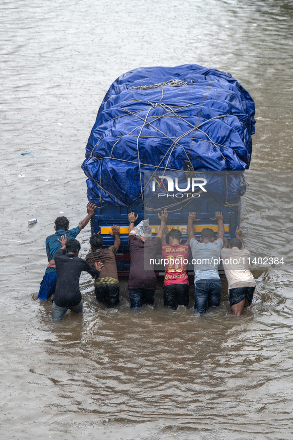 People are pushing a truck on a waterlogged street after heavy rain in Dhaka, Bangladesh, on July 12, 2024. 