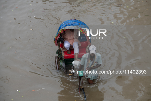 Passengers are riding on a rickshaw to go through a waterlogged street after heavy rain in Dhaka, Bangladesh, on July 12, 2024. 