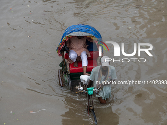 Passengers are riding on a rickshaw to go through a waterlogged street after heavy rain in Dhaka, Bangladesh, on July 12, 2024. (