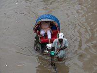 Passengers are riding on a rickshaw to go through a waterlogged street after heavy rain in Dhaka, Bangladesh, on July 12, 2024. (