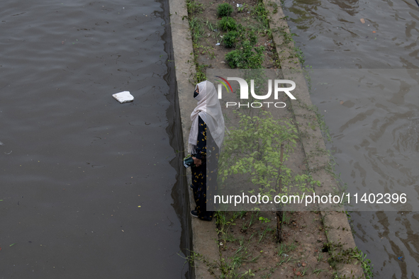 A woman is getting stuck on a road divider as she is being surrounded by a waterlogged street after heavy rain in Dhaka, Bangladesh, on July...