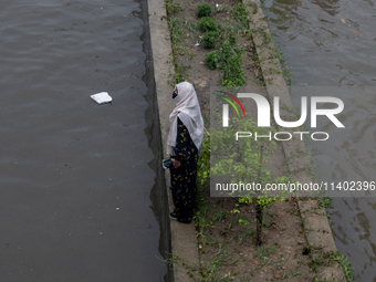 A woman is getting stuck on a road divider as she is being surrounded by a waterlogged street after heavy rain in Dhaka, Bangladesh, on July...