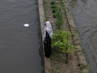 A woman is getting stuck on a road divider as she is being surrounded by a waterlogged street after heavy rain in Dhaka, Bangladesh, on July...