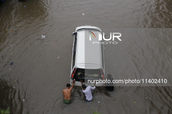 Men are pulling a vehicle through a flooded street after heavy monsoon rainfall in Dhaka, Bangladesh, on July 12, 2024. 