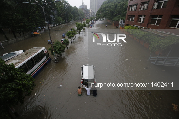 Men are pulling a vehicle through a flooded street after heavy monsoon rainfall in Dhaka, Bangladesh, on July 12, 2024. 