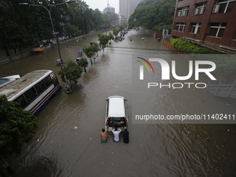 Men are pulling a vehicle through a flooded street after heavy monsoon rainfall in Dhaka, Bangladesh, on July 12, 2024. (