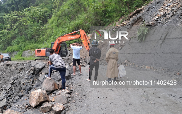 A worker is using an excavator to clear a landslide as local and other villagers, as well as workers, are watching boulders fallen from hill...