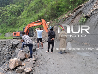 A worker is using an excavator to clear a landslide as local and other villagers, as well as workers, are watching boulders fallen from hill...