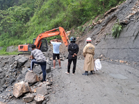 A worker is using an excavator to clear a landslide as local and other villagers, as well as workers, are watching boulders fallen from hill...