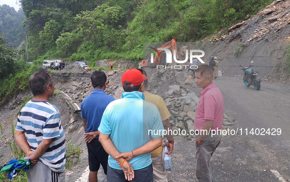 A worker is using an excavator to clear a landslide as local and other villagers, as well as workers, are watching boulders fallen from hill...