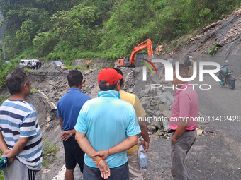 A worker is using an excavator to clear a landslide as local and other villagers, as well as workers, are watching boulders fallen from hill...