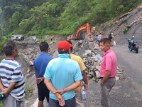 A worker is using an excavator to clear a landslide as local and other villagers, as well as workers, are watching boulders fallen from hill...