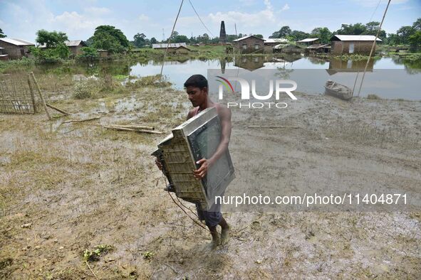 An Indian man is carrying a television set in the flood-affected Jakhalabandha in Nagaon District of Assam, India, on July 13, 2024. 