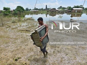 An Indian man is carrying a television set in the flood-affected Jakhalabandha in Nagaon District of Assam, India, on July 13, 2024. (