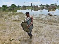 An Indian man is carrying a television set in the flood-affected Jakhalabandha in Nagaon District of Assam, India, on July 13, 2024. (