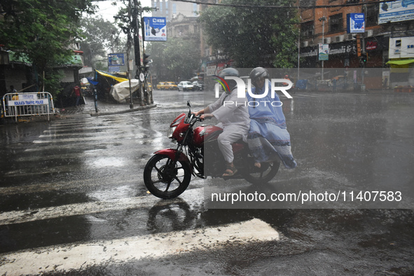 People are riding on a motorcycle during the heavy rain in Kolkata, India, on July 14, 2024. 