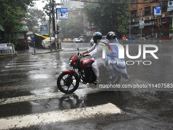 People are riding on a motorcycle during the heavy rain in Kolkata, India, on July 14, 2024. (