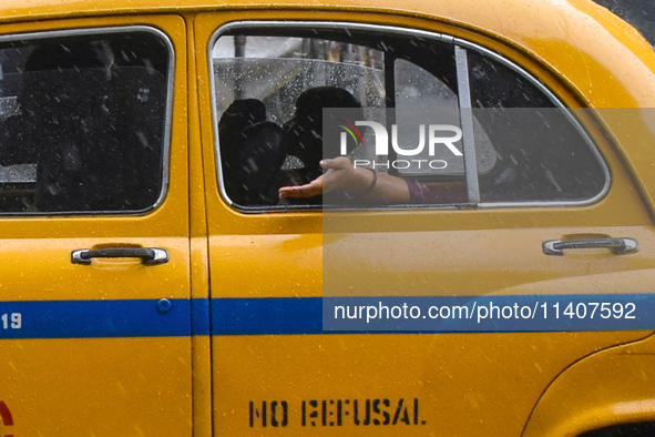 A woman is feeling the rain from a taxi during the heavy rain in Kolkata, India, on July 14, 2024. 