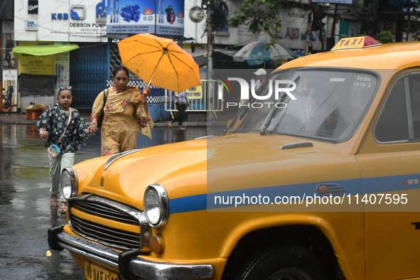 A lady with a girl is holding an umbrella while crossing a street during the heavy rain in Kolkata, India, on July 14, 2024. 