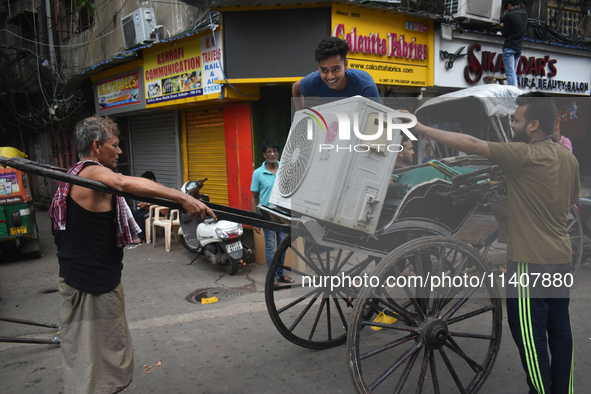 People are carrying an air conditioner into a hand-pulled rickshaw on a hot day in Kolkata, India, on July 14, 2024. 