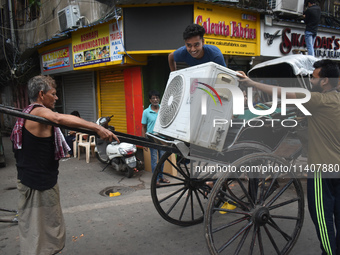 People are carrying an air conditioner into a hand-pulled rickshaw on a hot day in Kolkata, India, on July 14, 2024. (