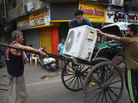 People are carrying an air conditioner into a hand-pulled rickshaw on a hot day in Kolkata, India, on July 14, 2024. (