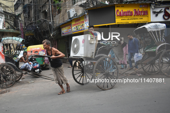 People are carrying an air conditioner into a hand-pulled rickshaw on a hot day in Kolkata, India, on July 14, 2024. 