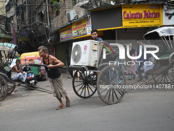 People are carrying an air conditioner into a hand-pulled rickshaw on a hot day in Kolkata, India, on July 14, 2024. (