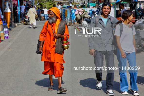 A sadhu is walking past a young couple along Mall Road in Mussoorie, Uttarakhand, India, on April 18, 2024. 