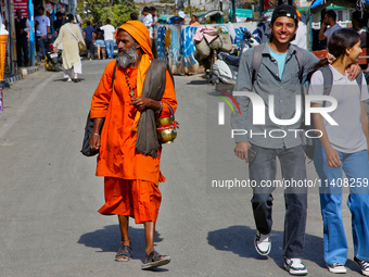 A sadhu is walking past a young couple along Mall Road in Mussoorie, Uttarakhand, India, on April 18, 2024. (