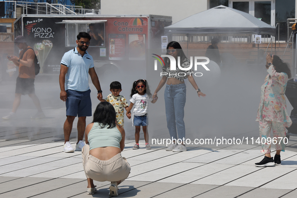 People are cooling off during a hot summer afternoon as they walk amongst water vapor being sprayed from the ground in Toronto, Ontario, Can...