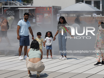 People are cooling off during a hot summer afternoon as they walk amongst water vapor being sprayed from the ground in Toronto, Ontario, Can...