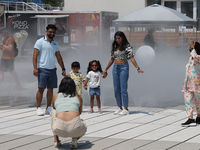 People are cooling off during a hot summer afternoon as they walk amongst water vapor being sprayed from the ground in Toronto, Ontario, Can...