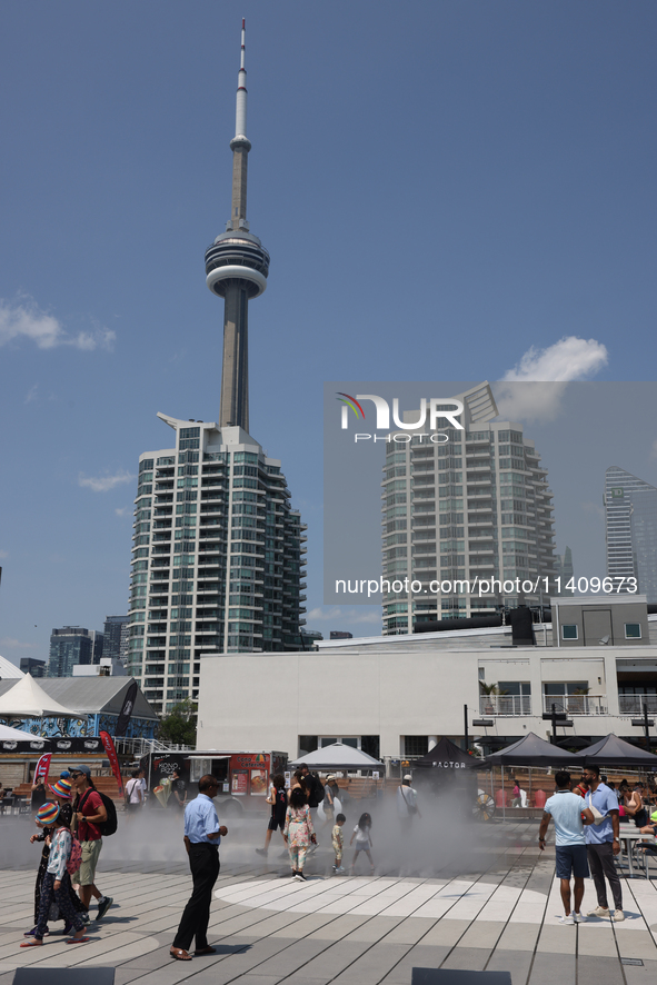 People are cooling off during a hot summer afternoon as they walk amongst water vapor being sprayed from the ground in Toronto, Ontario, Can...