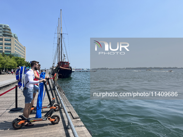 People are riding scooters along the boardwalk at Harbourfront in Toronto, Ontario, Canada, on July 13, 2024. 