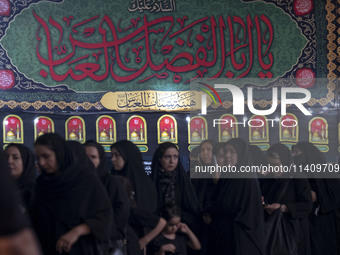 Veiled women are standing in line while waiting to receive donated meals and participating in a religious rally to commemorate Tasoua, in Do...