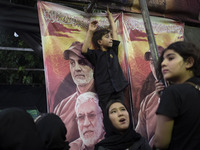 A young boy is standing in front of a banner featuring portraits of the former commander of the Hashd Shabi, Abu Mahdi al-Muhandes (bottom),...