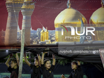 Young boys are standing under a religious banner while they are participating in a religious rally to commemorate Tasoua, in Dolatabad neigh...