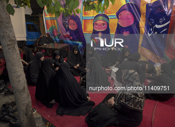 Veiled Iranian women are sitting together in front of a banner featuring cartoon faces of veiled young girls, during a religious rally to co...