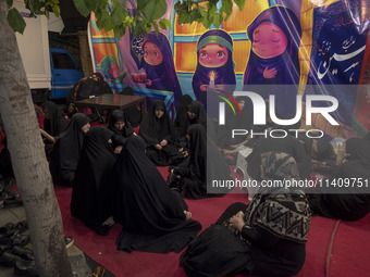 Veiled Iranian women are sitting together in front of a banner featuring cartoon faces of veiled young girls, during a religious rally to co...