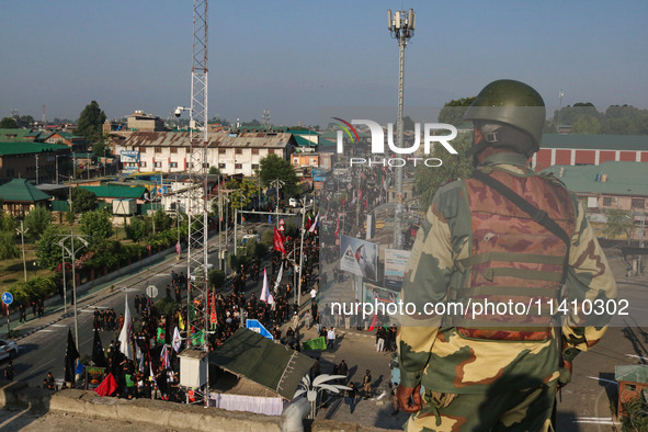 An Indian security personnel is standing guard as Kashmiri Shiite Muslim mourners are taking part in a Muharram procession on the eighth day...