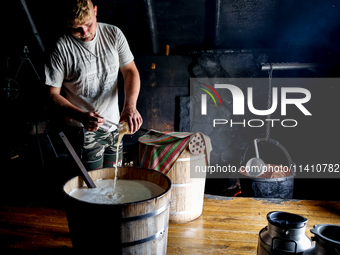 Piotr, son of Baca Krzysztof Las (a traditional Polish Carpathian mountains shepherd) prepares sheep milk to make cheese in Traditional wood...