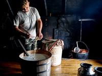 Piotr, son of Baca Krzysztof Las (a traditional Polish Carpathian mountains shepherd) prepares sheep milk to make cheese in Traditional wood...