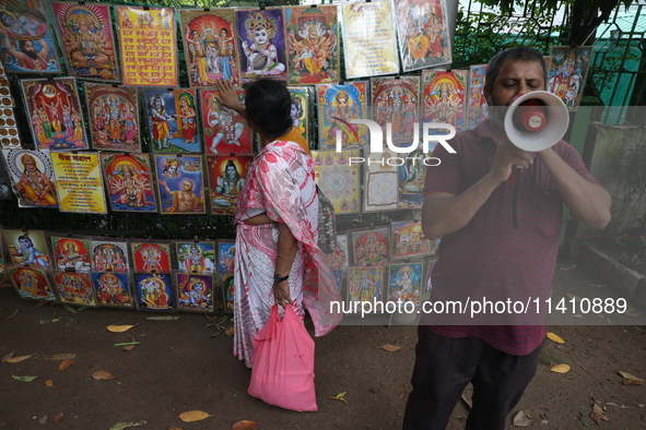 A Hindu devotee is seeking blessings from a picture as a man is using a megaphone to sell Hindu God and Goddess images on the last day of th...