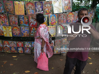 A Hindu devotee is seeking blessings from a picture as a man is using a megaphone to sell Hindu God and Goddess images on the last day of th...