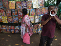 A Hindu devotee is seeking blessings from a picture as a man is using a megaphone to sell Hindu God and Goddess images on the last day of th...